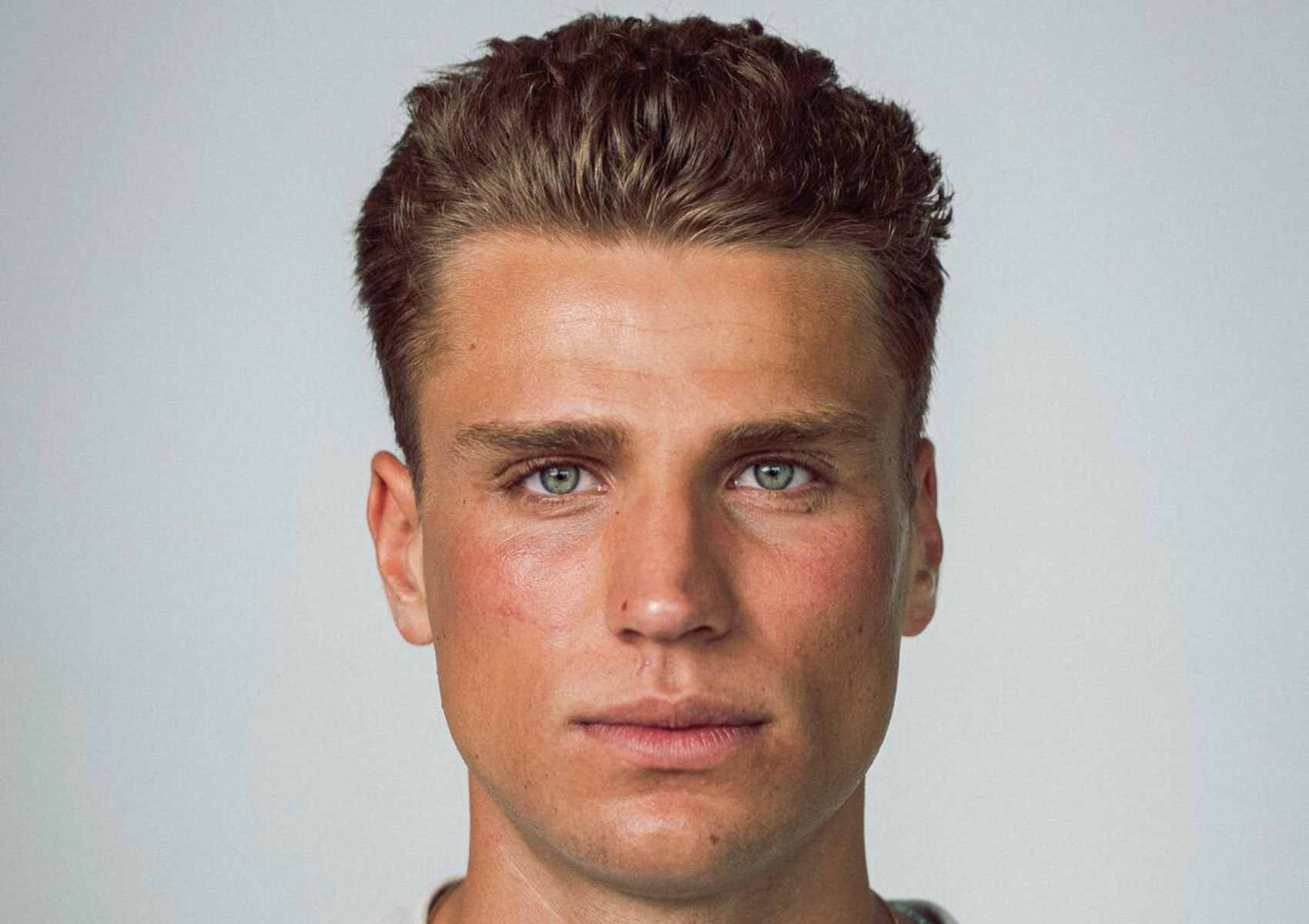 Porträt eines jungen Mannes mit markanten Gesichtszügen, grünen Augen und gepflegter Haut – Nahaufnahme mit neutralem Gesichtsausdruck vor hellem Hintergrund